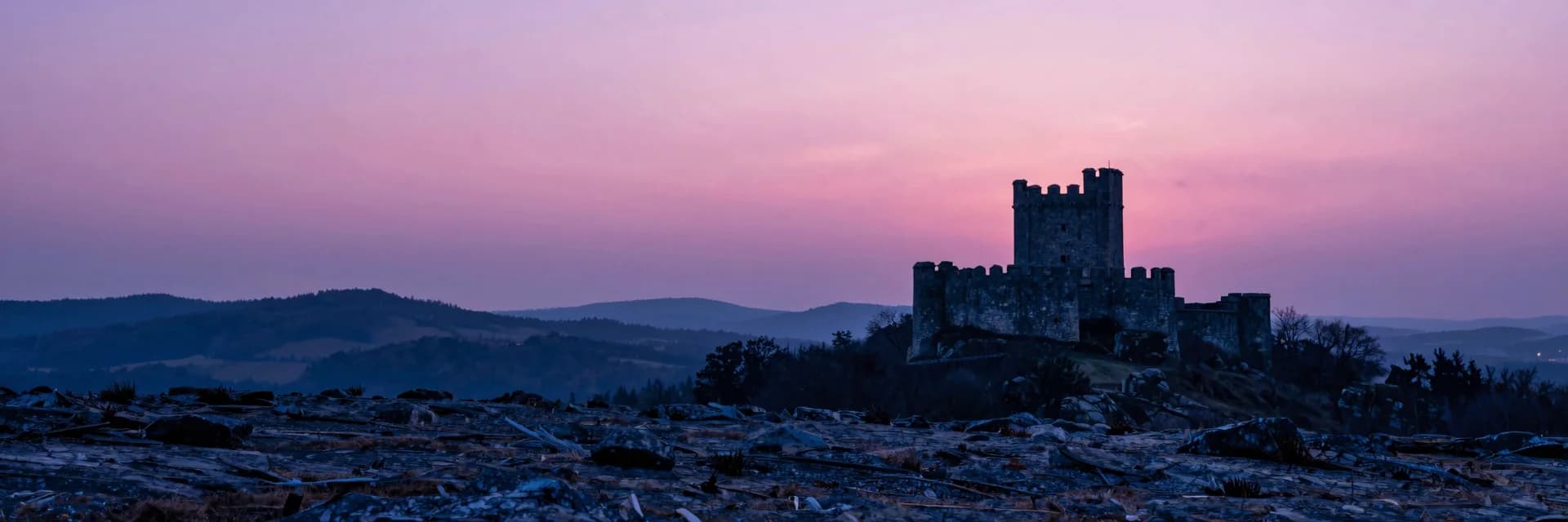 Distant medieval castle silhouetted small in the right third, perched on a ridge at dusk, dwarfed by a vast pink-purple sky filling the upper two-thirds.