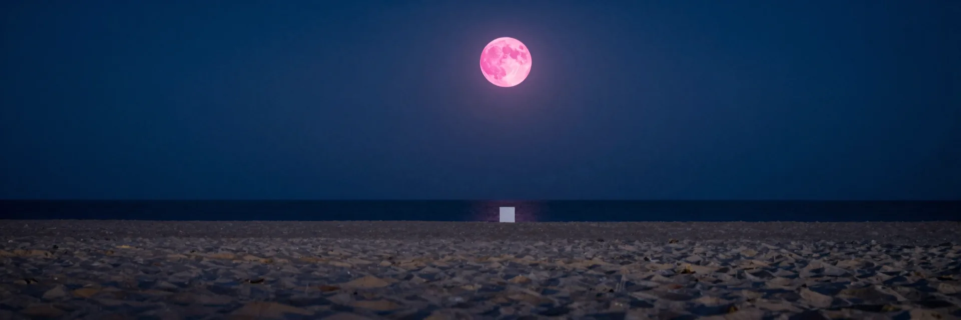 An ultra-wide vista of vast beach at night, the cube small in the landscape beneath a prominent pink moon.