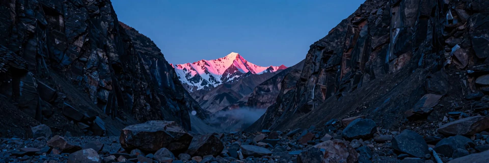 Ultra-wide view of a deep rocky canyon opening framing a distant snow-capped mountain with a tiny castle silhouette at the canyon mouth at sunset.