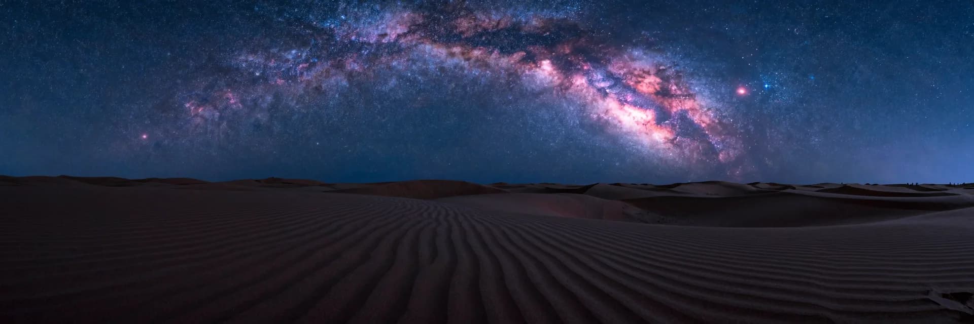 Ultra-wide view of dunes receding to the vanishing point under a galactic sky.