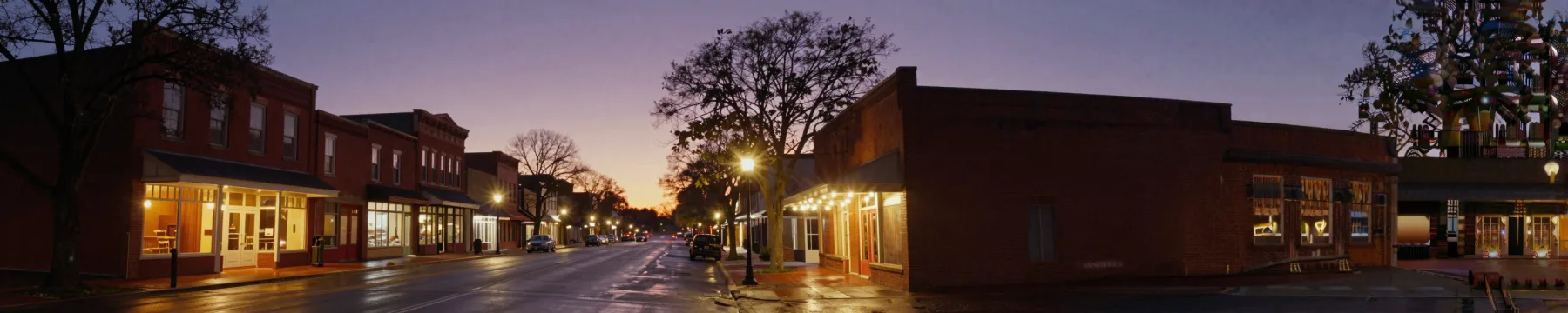 A downtown North Carolina main street at twilight, storefronts lit warm under a purple sky.